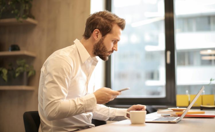 Afbeelding man aan bureau met telefoon en laptop